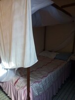 A single bed with a canopy, a patterned bedspread, and a striped rug on the floor.