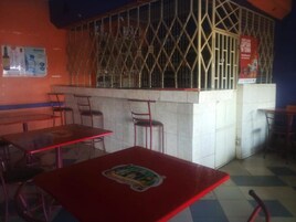 A restaurant interior with red tables and chairs, a tiled floor, and a counter with a metal grill.