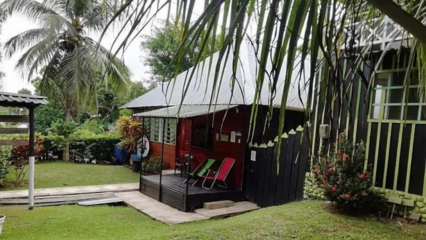 Una casa petita amb un porxo, envoltada d'un jardí ben cuidat i palmeres.