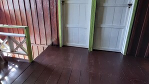 Una habitació amb sòl de fusta, dues portes blanques amb detalls verds i una banca de fusta.