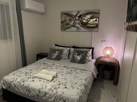 Un dormitorio con cama, aire acondicionado de pared, lámpara decorativa y un cuadro.
