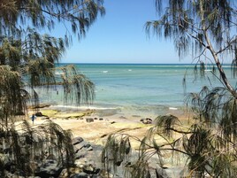 Una playa con agua turquesa cristalina, rodeada de terreno rocoso y vegetación escasa.
