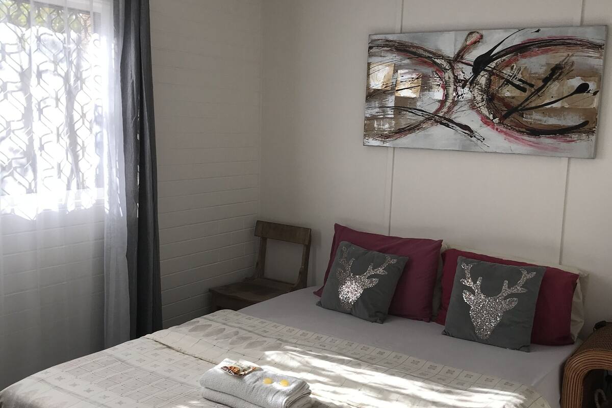 A bedroom with a bed, a ceiling fan, a window with curtains, and a wall-mounted abstract painting.