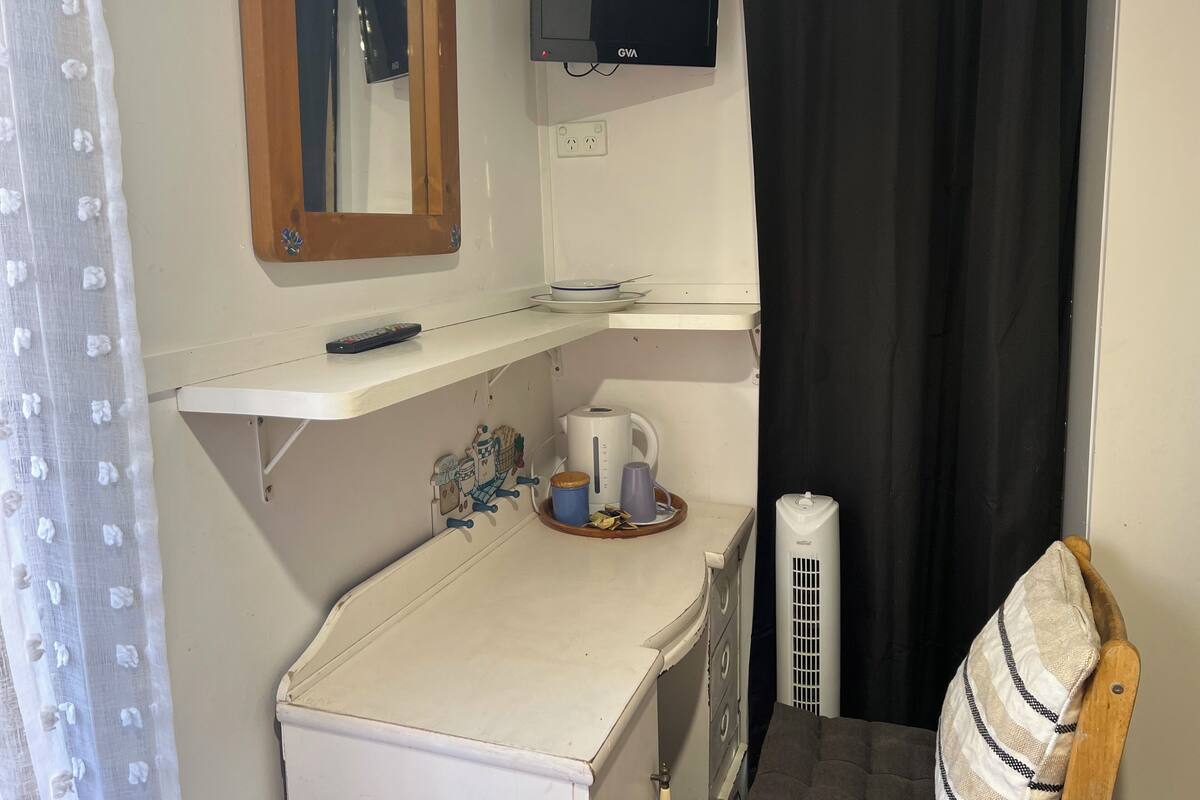 A compact bathroom with a white sink, a mirror, a GVA brand TV mounted above, a small shelf with a remote control, a kettle, and a radiator.