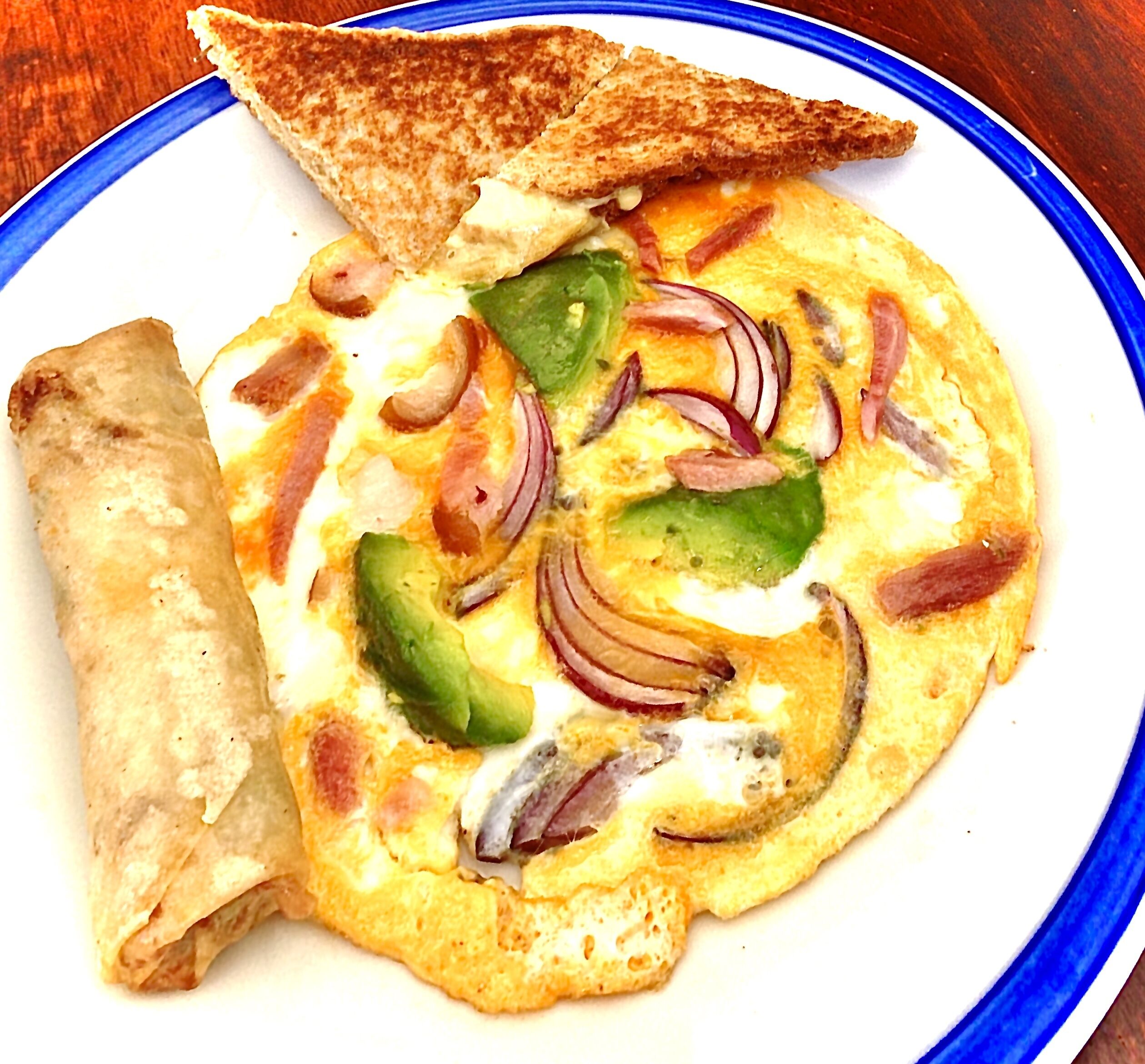 A plate with an omelette, green peppers, red onions, and a piece of toast.
