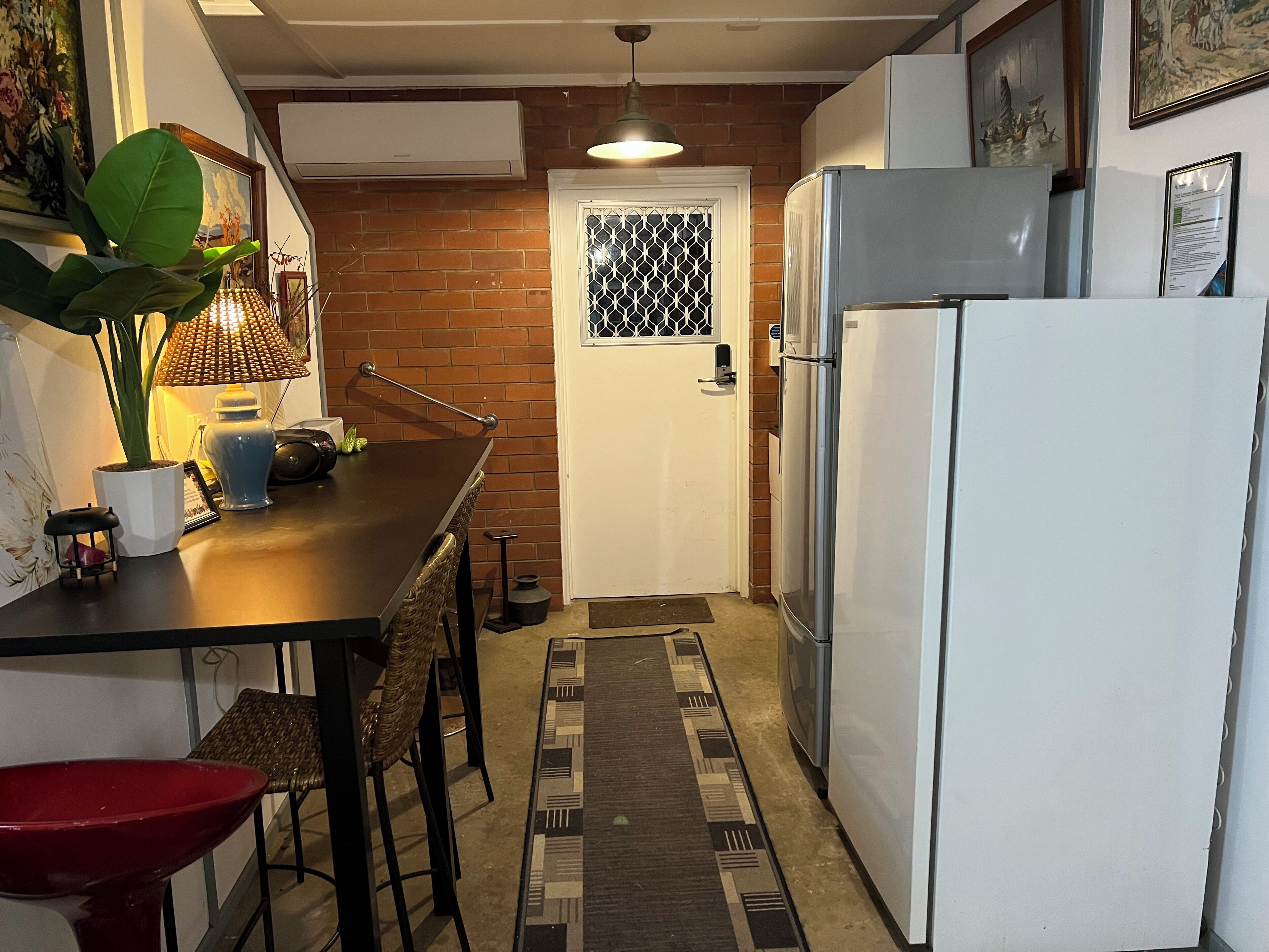 Een kleine keuken met een koelkast, een eettafel met stoelen, een potplant en een kamerkleed met een patroon.