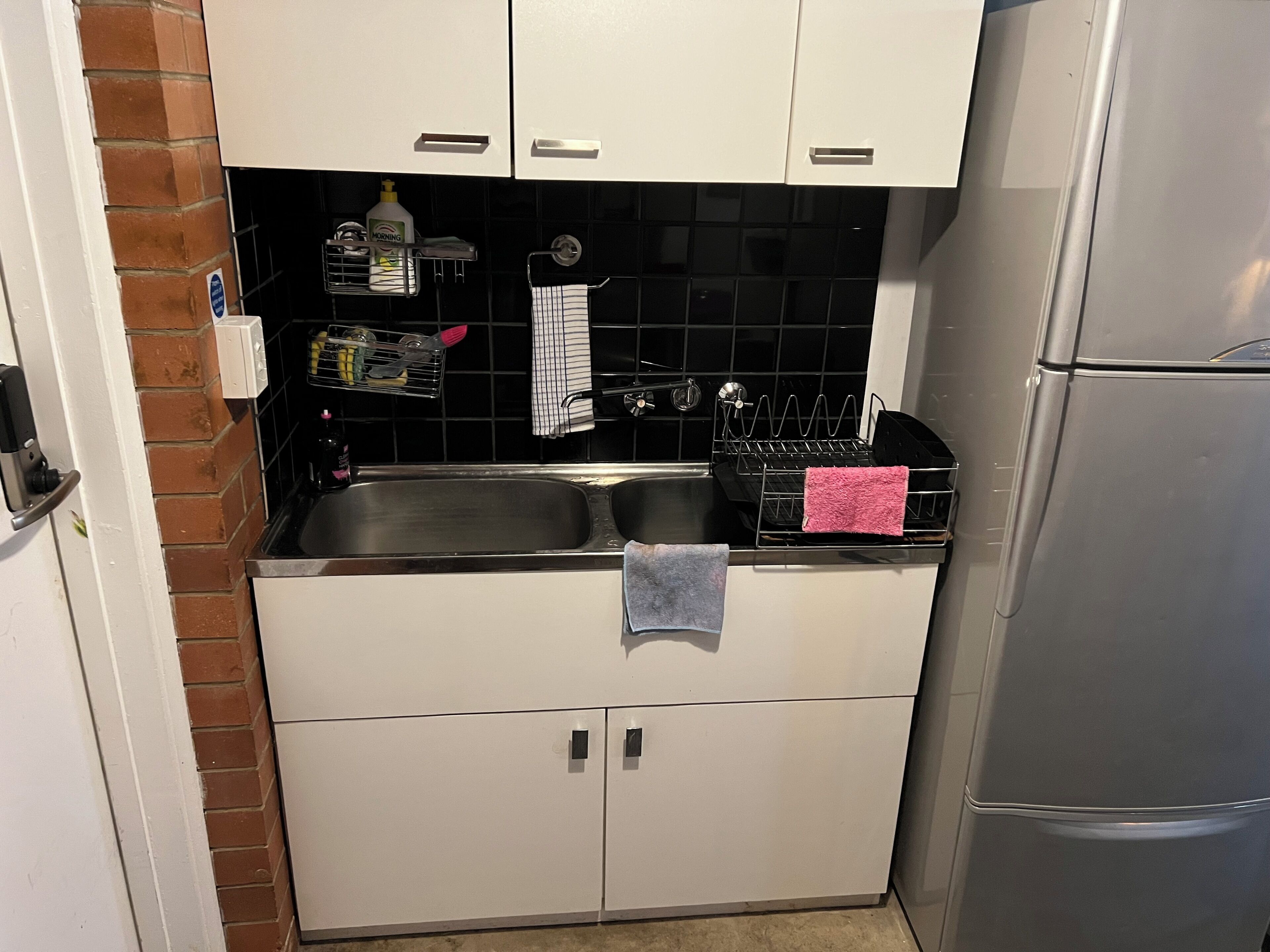 Una cucina compatta con lavello in acciaio inox, mobili bianchi e forno integrato.