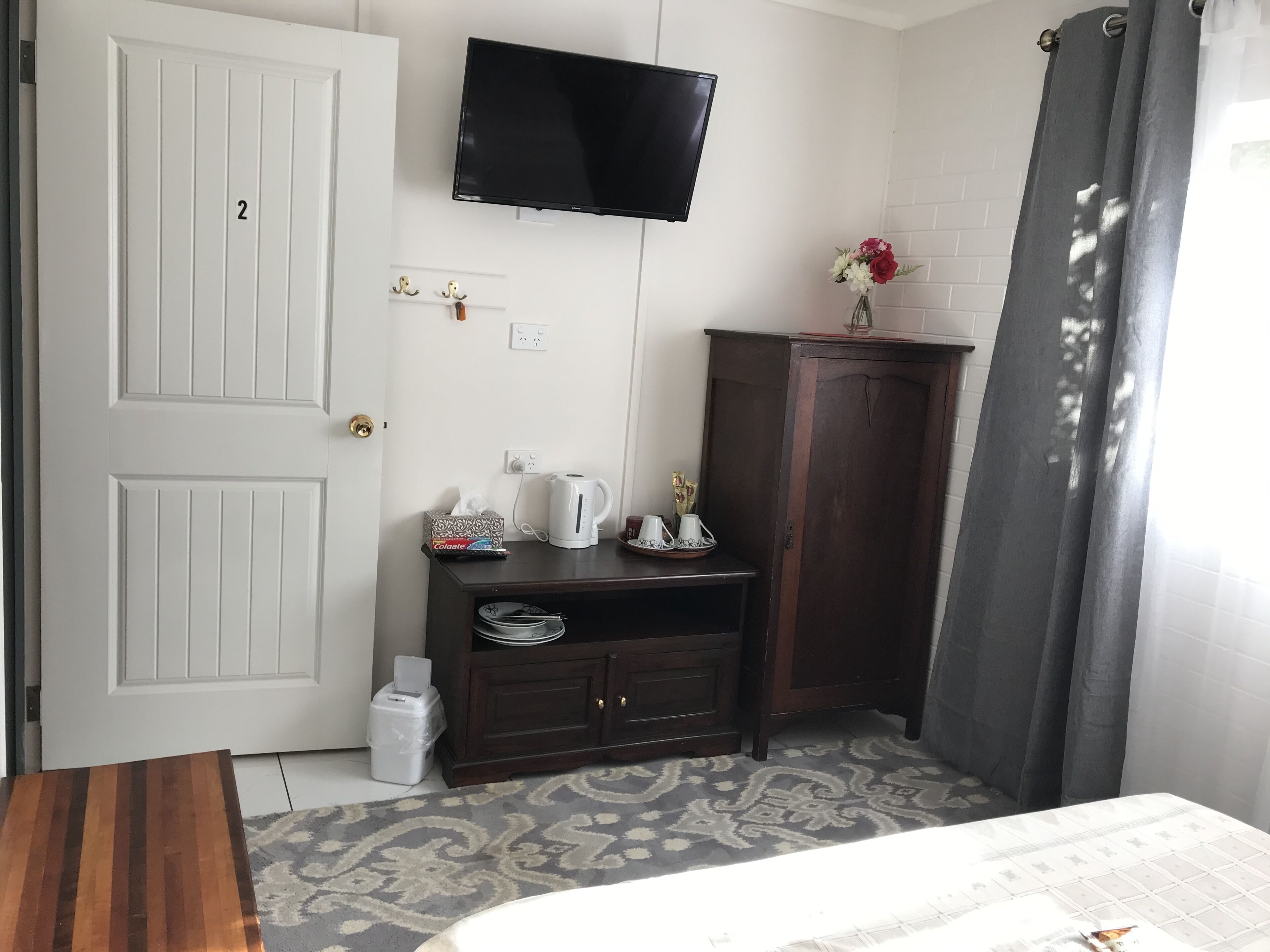 Ein Hotelzimmer mit einem Bett, einem an der Wand befestigten Fernseher, einem Schrank mit Toilettenartikeln und einem gemusterten Teppich.