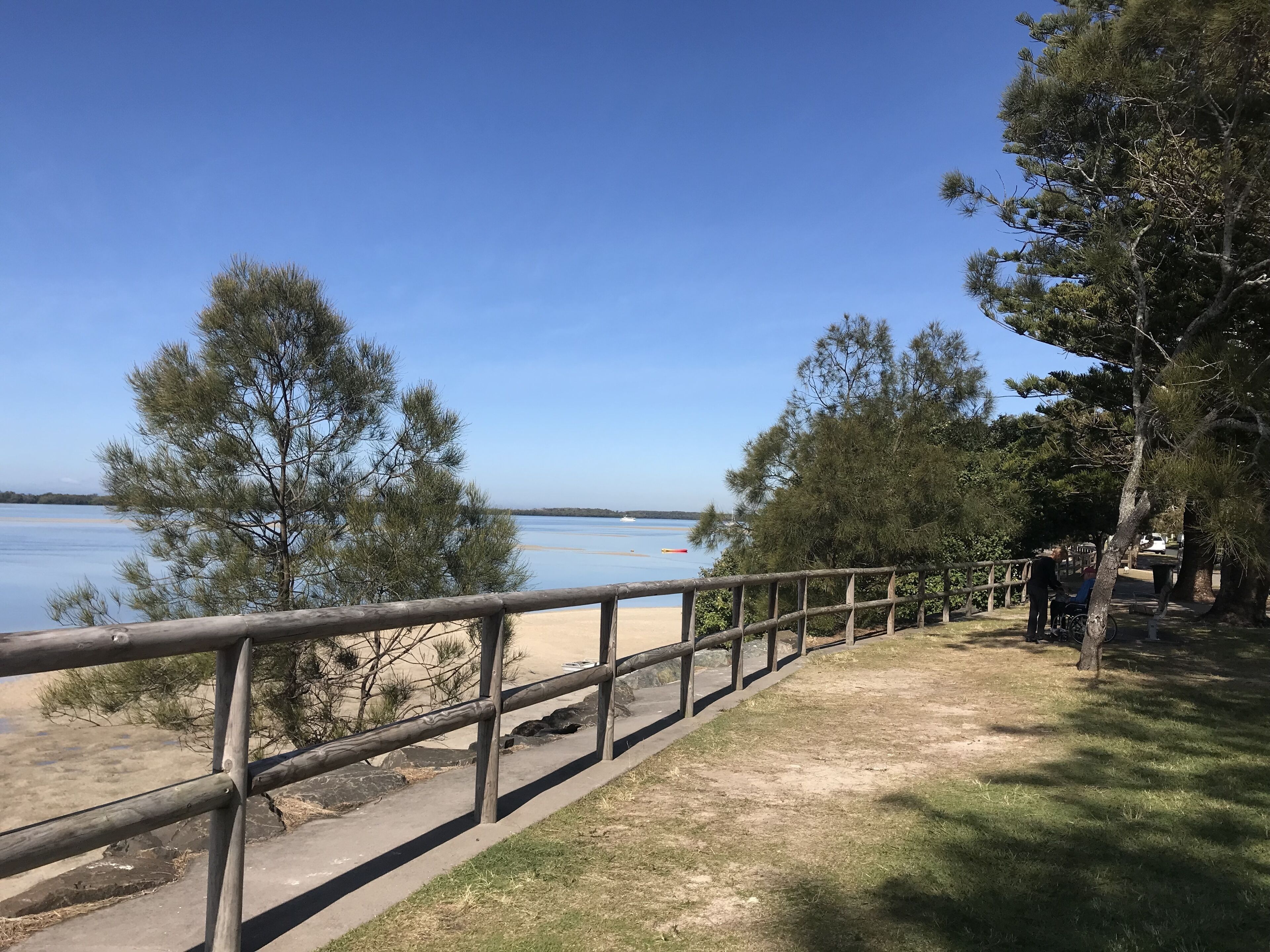 Ett trästaket med utsikt över en strand, med träd och en klar himmel.