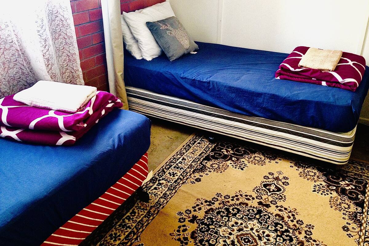 A room with two beds, a patterned rug, and a window with curtains.
