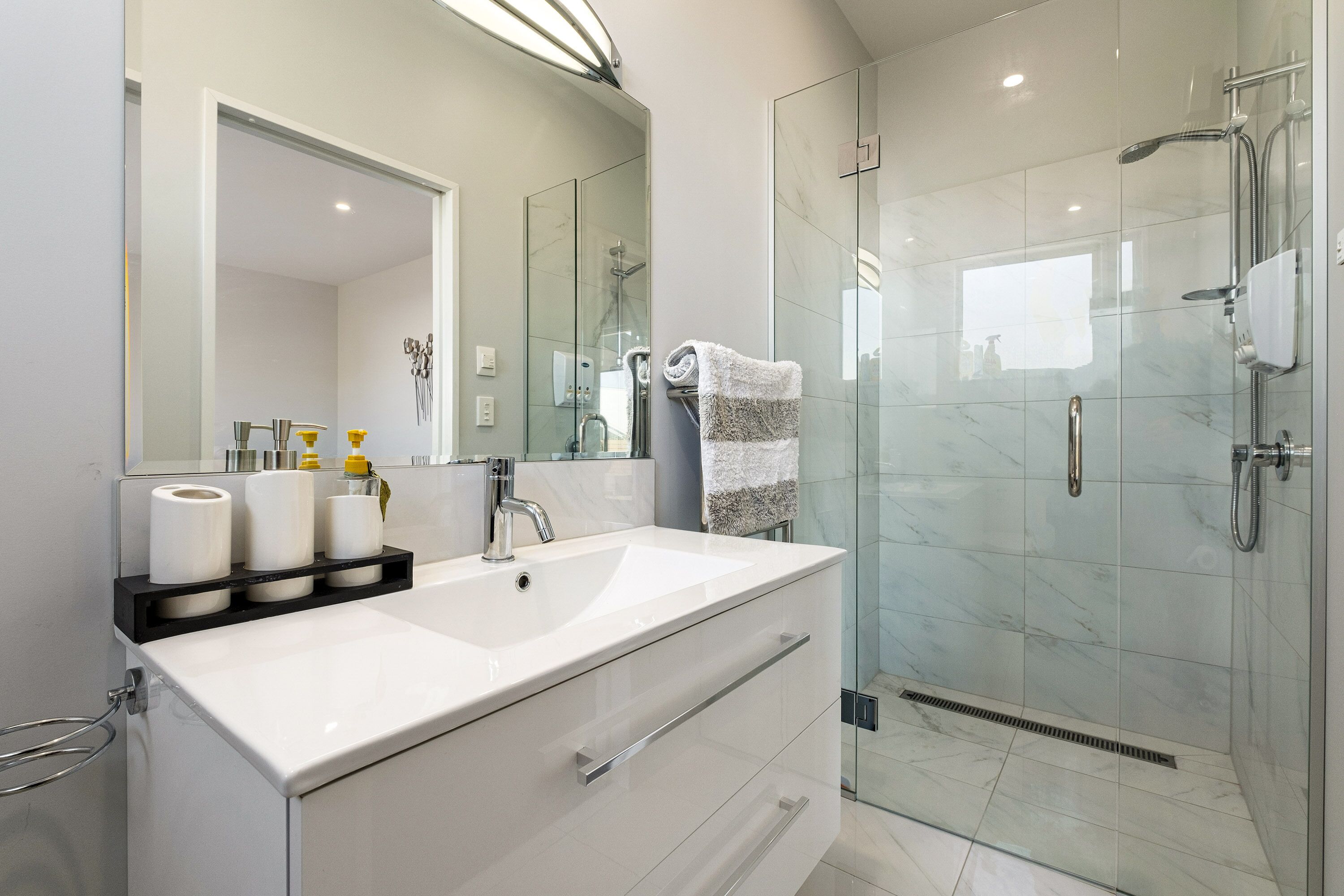 A modern bathroom with a white sink, mirror, and glass shower enclosure.