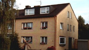 A two-story brick apartment with multiple windows, a visible satellite dish, and a small garden area with flowers. - Pension Doemens (Aachen)