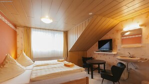 A bedroom with a bed, a TV, a small table, a chair, and a sink. - Pension Doemens (Aachen)