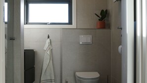 Un baño moderno con inodoro, una toalla colgada en la pared, una planta en maceta y una ventana sobre el inodoro.
