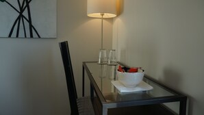 Una habitación moderna con una mesa de vidrio, un tazón blanco con aperitivos, una lámpara y un cuadro en la pared.