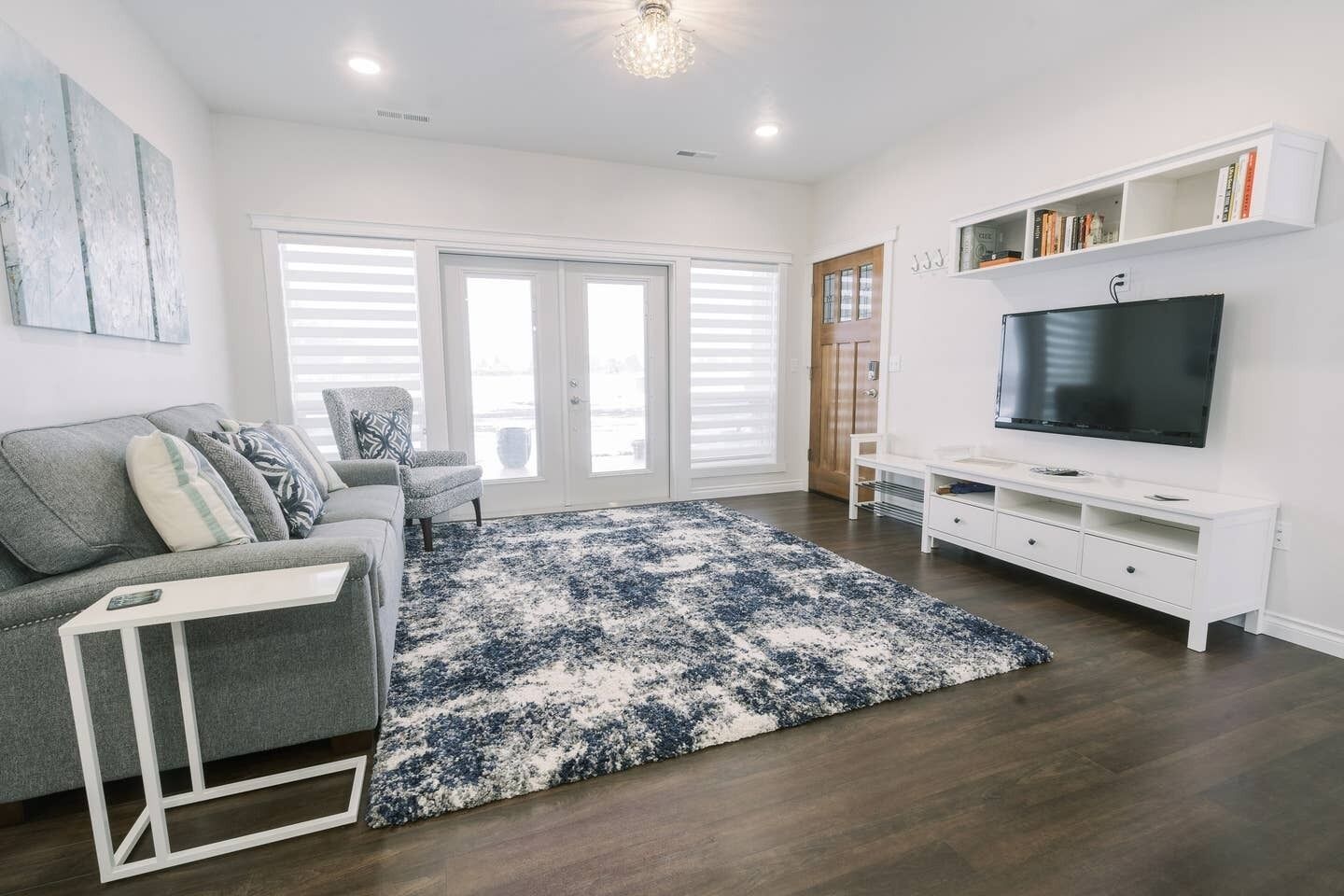 Una sala moderna con un sofá gris, un mueble de televisión blanco y un tapete grande azul y blanco.