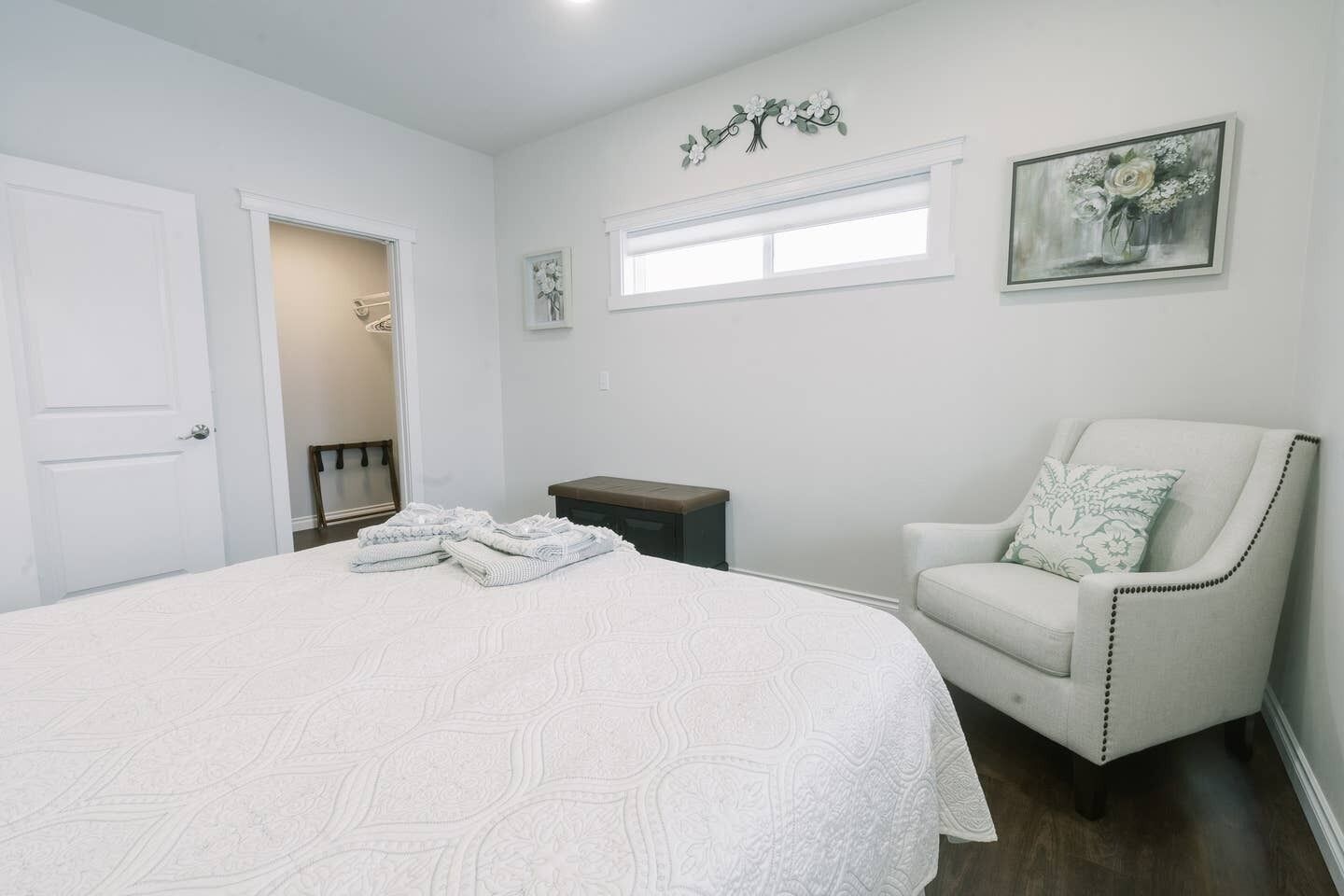 A bedroom with a large bed, a chair, a nightstand, and a window.