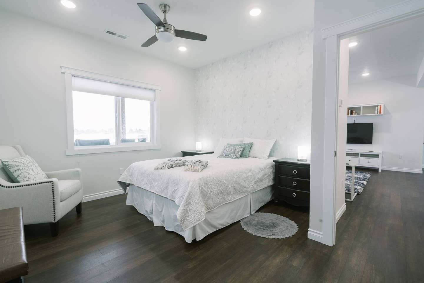A bedroom with a bed, a chair, a nightstand, a TV, and a ceiling fan.