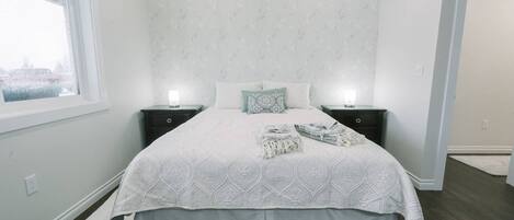Una cama bien hecha con una colcha estampada, dos mesitas de noche con lámparas y una ventana con vistas.