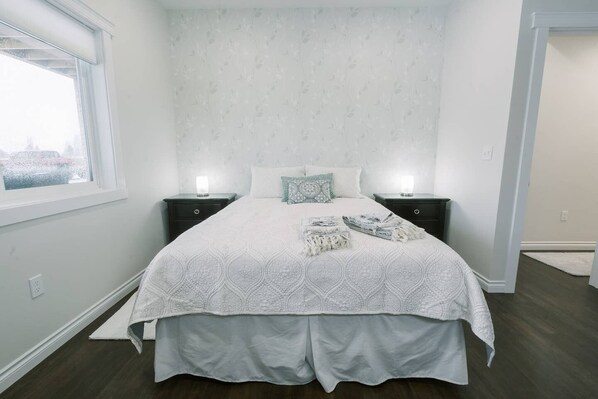 A neatly made bed with a patterned bedspread, two bedside tables with lamps, and a window with a view. - Beautiful Master Suite & Full Kitchen in New Home (Spokane)
