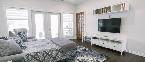 A modern bedroom with a bed, a TV, a bookshelf, and a large window.