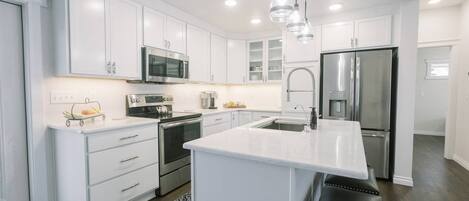 Una cocina moderna con armarios blancos, electrodomésticos de acero inoxidable e iluminación colgante.