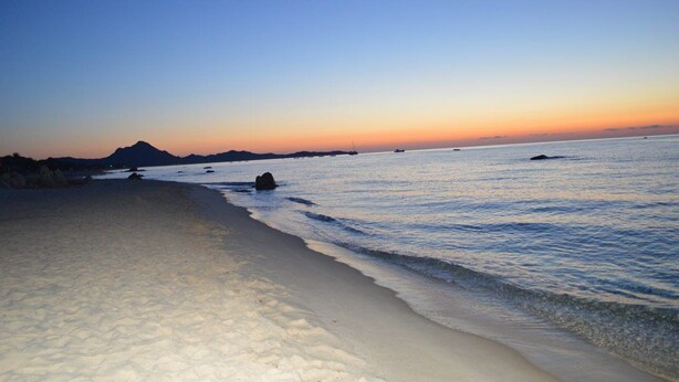 Ein Strand mit ruhigem Wasser, blauem Himmel und Bergen in der Ferne.