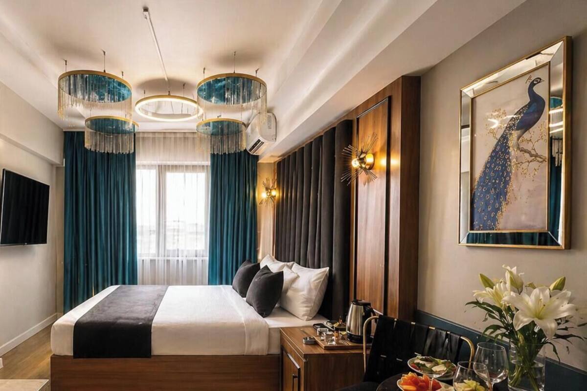 Een hotelkamer met een groot bed, een eettafel met stoelen, een spiegel en een schilderij van een pauw aan de muur.
