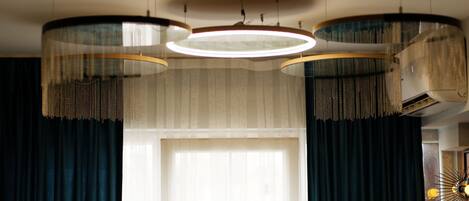 A room with a large window, dark curtains, and a circular ceiling light fixture.