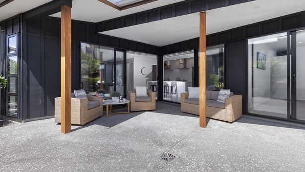 Un espace de vie extérieur moderne, doté de meubles en osier et d’un patio couvert.