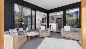 Un espace extérieur moderne, aménagé avec des meubles en osier et une petite table, et de grandes portes vitrées donnant sur une cuisine et un coin repas.