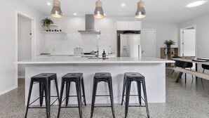 Une cuisine moderne dotée d’un îlot central, de tabourets de bar, de luminaires suspendus et d’un coin repas avec une table et des chaises.