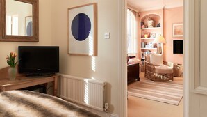 A hotel room with a television, a mirror, a framed artwork, a wicker chair, and a lamp. - A PERFECT TREASURE -  KNIGHTSBRIDGE LUXURY MEWS APARTMENT (London)