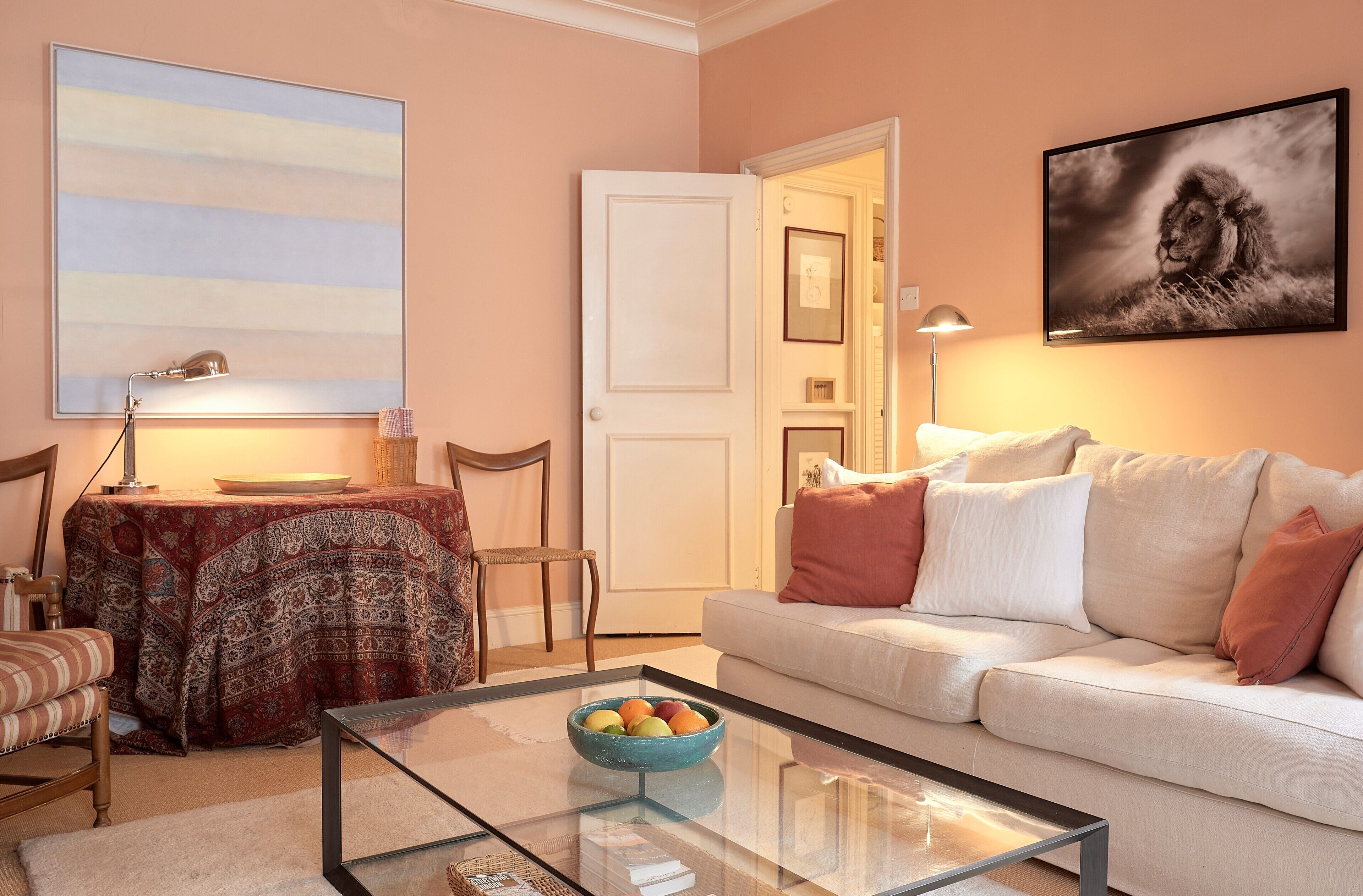 A living room with a sofa, a glass coffee table with a fruit bowl, a patterned tablecloth, and a wall-mounted picture.