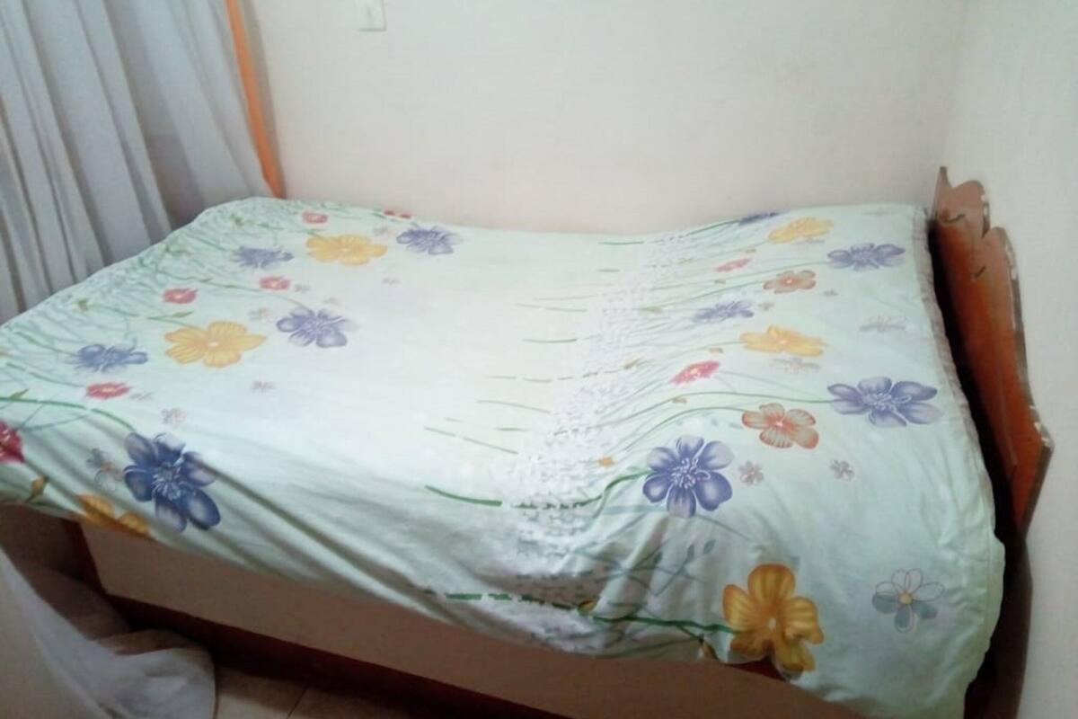 A single bed with a floral bedspread in a room with a plain wall and a curtain.
