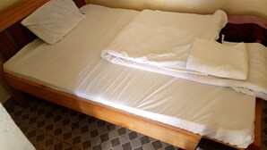 A small, single-bed room with a wooden headboard, a plain white mattress, and a simple, unadorned wall. - Silverstone Park Bar & Guest House (Nairobi)
