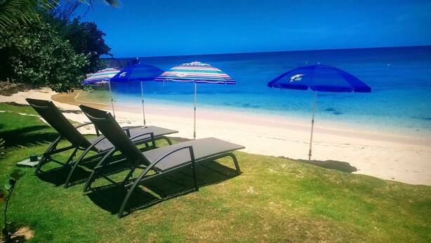 A beach with lounge chairs and striped umbrellas. - Beachcliff Villa Negril (Negril)