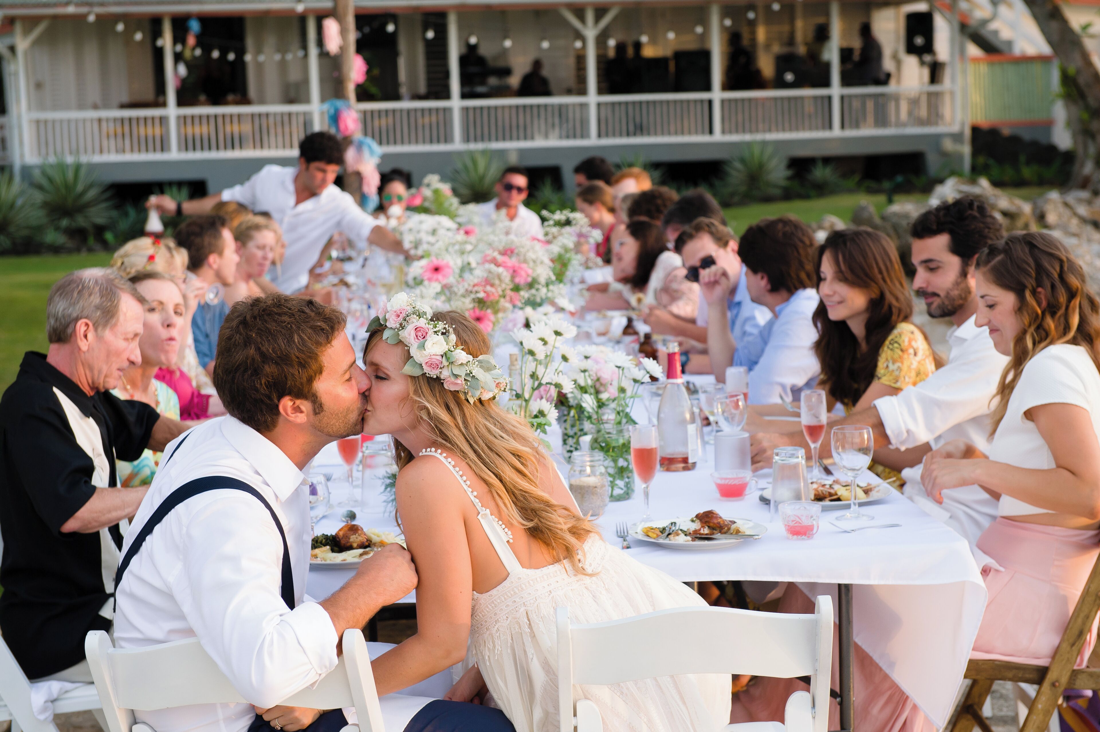 Una recepción de boda con invitados sentados en mesas redondas, decoradas con centros de flores y manteles blancos.
