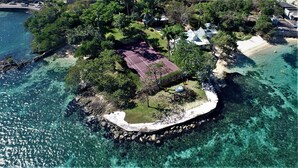 An aerial view of a small island with clear turquoise waters, surrounded by lush greenery and a few buildings. - Beachcliff Villa Negril (Negril)
