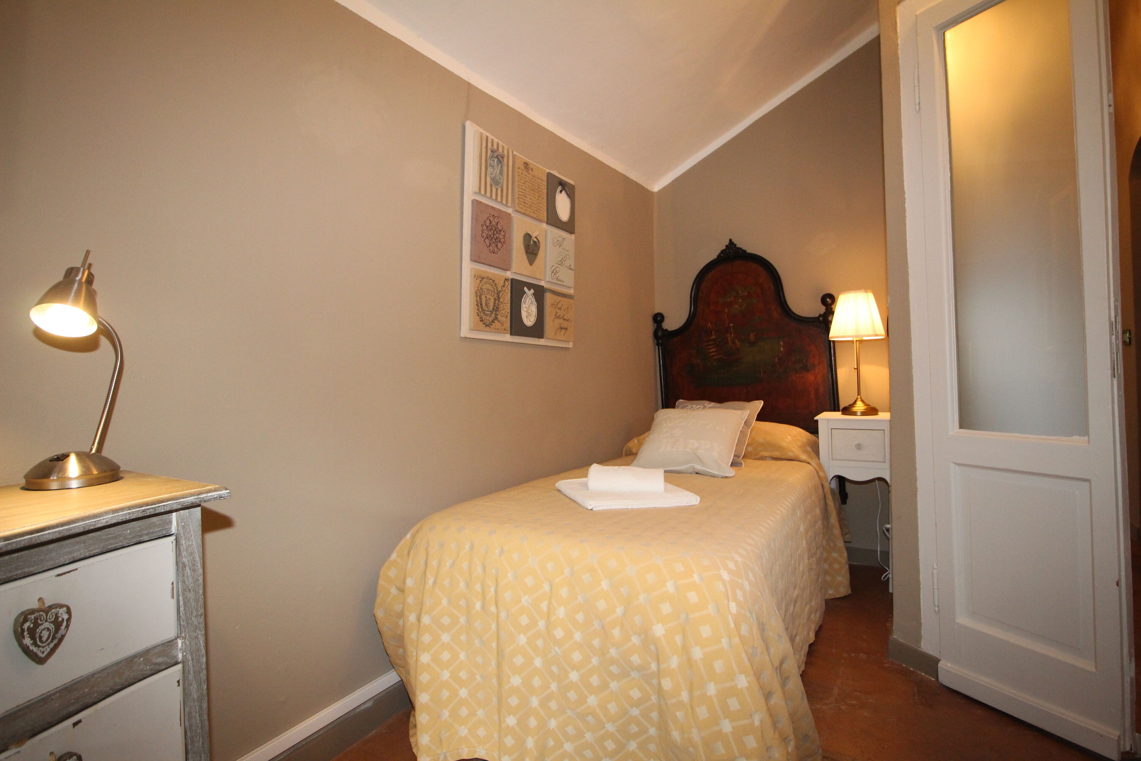 A bedroom with a bed, bedside table, lamp, and wall art.