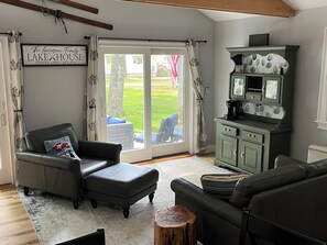 Una sala de estar con un sofá, una silla, una mesa de centro, un mueble aparador y un vidrio corredizo que da a un patio.