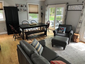 A living room with a dark wooden dining table, black chairs, a leather sofa, and a large window with a view of the outdoors. - 3 bedroom, 2 Baths, 8 Sleeps, detached bunk house, open boat slip (Ossipee, NH 03814)