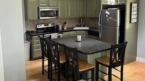 A modern kitchen with green cabinets, a central island with chairs, a refrigerator, and a microwave. - 3 bedroom, 2 Baths, 8 Sleeps, detached bunk house, open boat slip (Ossipee, NH 03814)