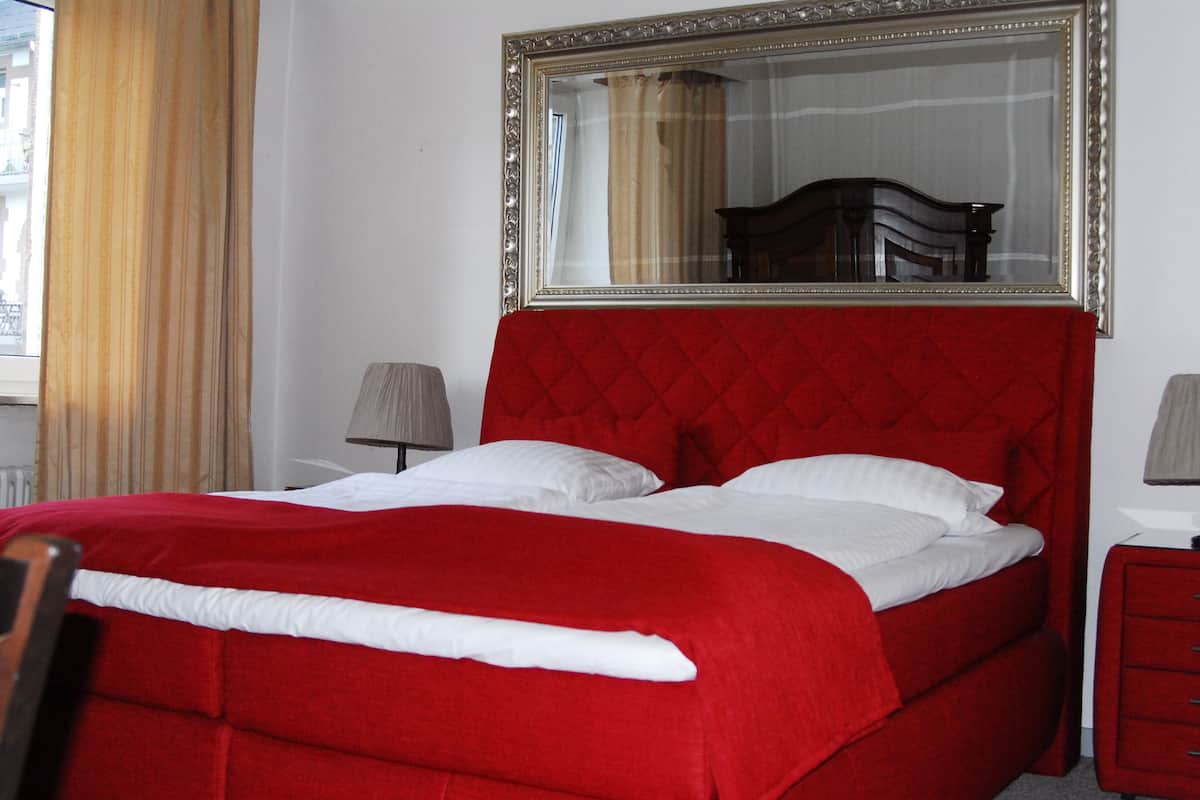 Una cama con cabecera acolchada roja, ropa de cama blanca y un espejo grande encima.