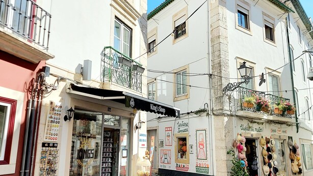 Una strada acciottolata con negozi, tra cui un negozio di cappelli e un altro con un cartello che recita "King's Shop".