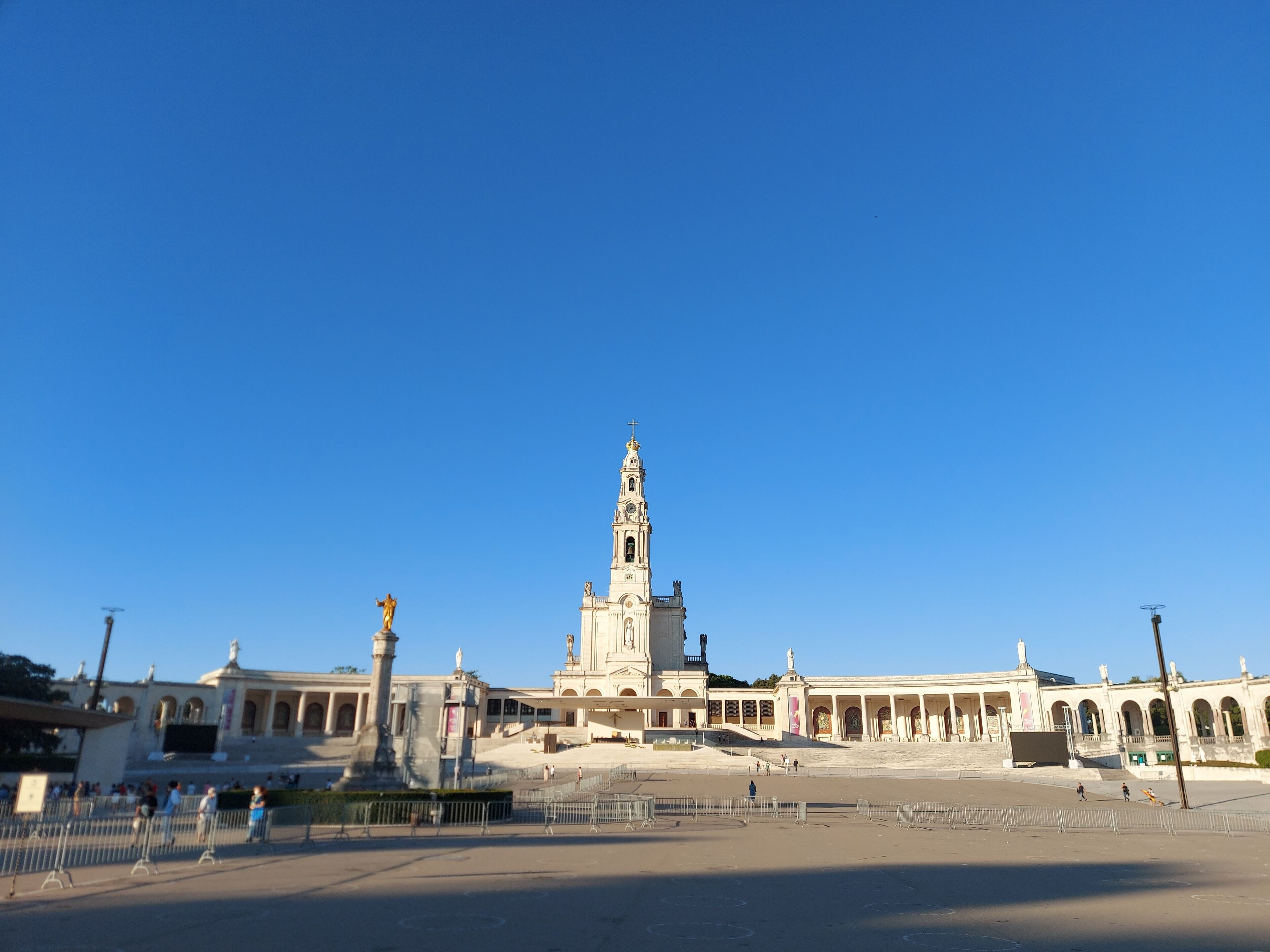 Una amplia plaza abierta con un edificio blanco destacado, que cuenta con una torre alta y estatuas.