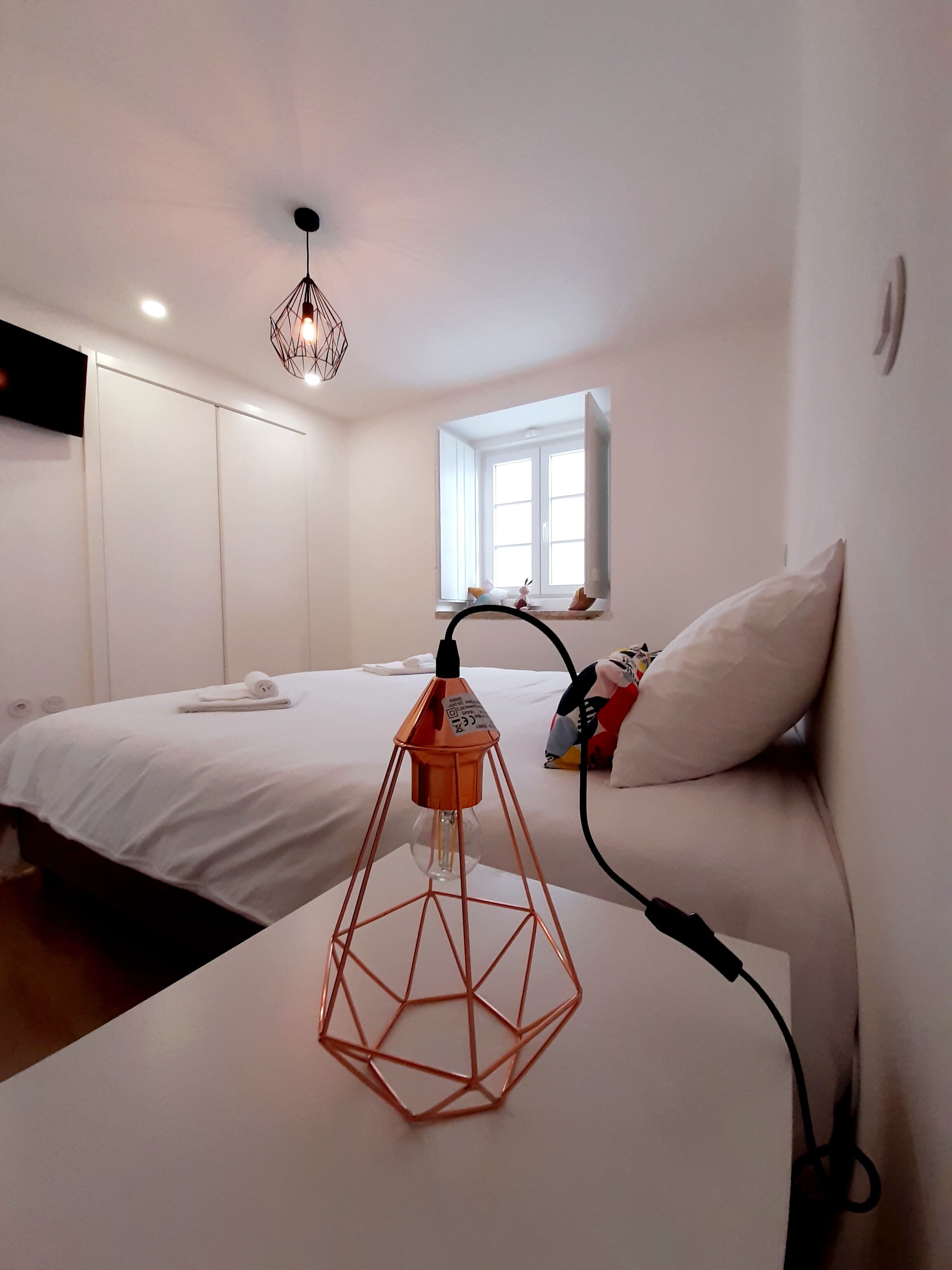 Une chambre d’hôtel moderne avec un lit, un canapé blanc, une lampe au design géométrique et une fenêtre donnant sur un paysage agréable.