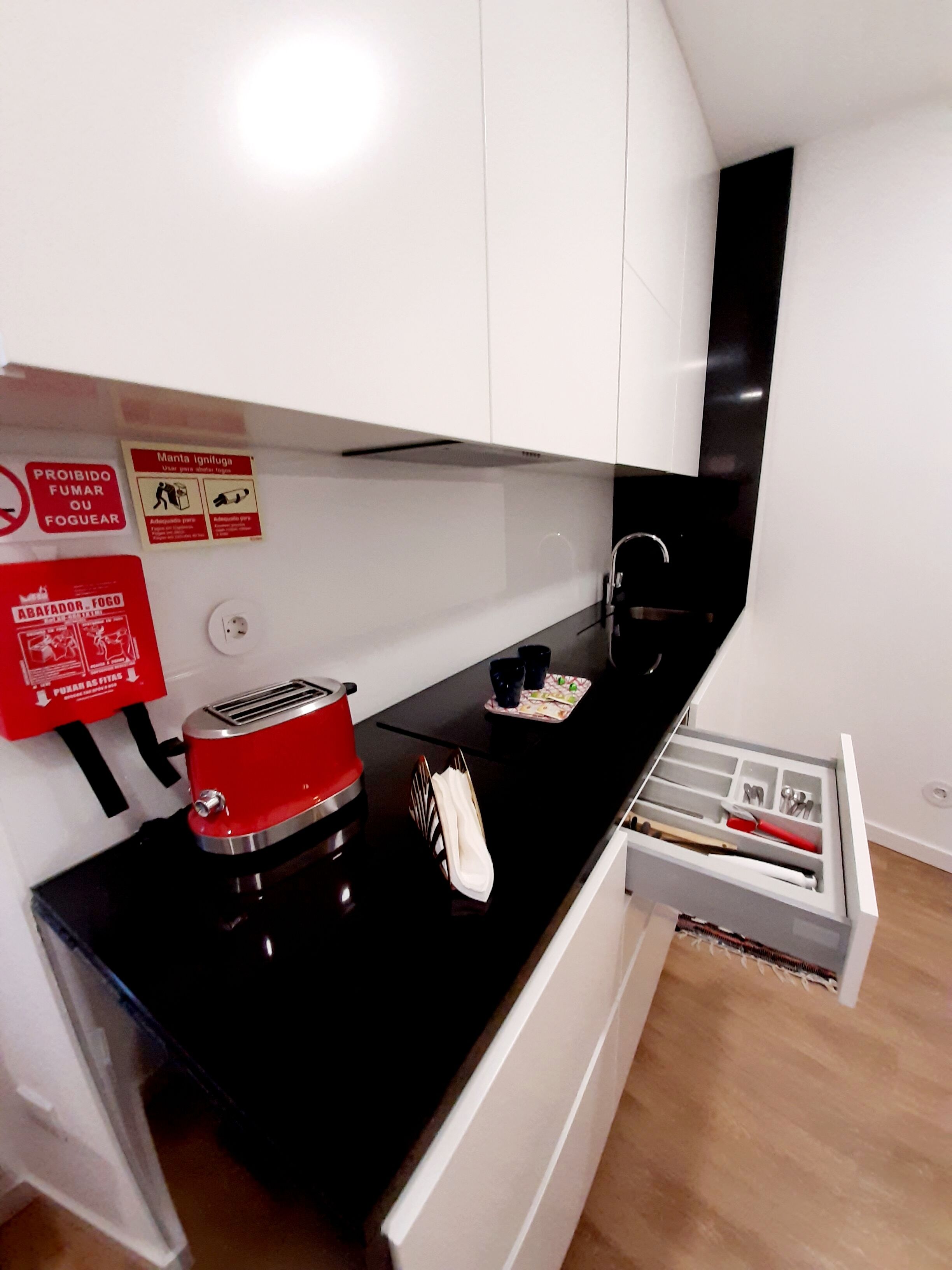 Una cocina moderna con armarios blancos, una encimera negra, un tostador rojo y un cajón con utensilios.