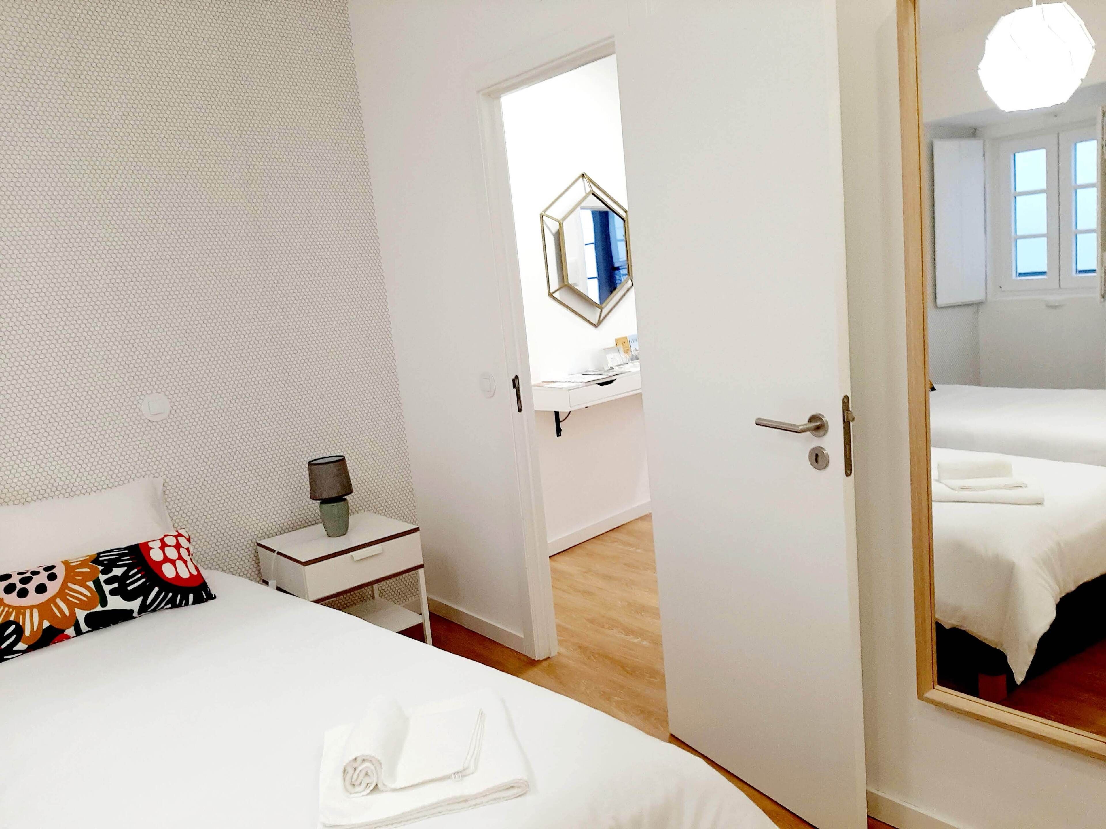 Une chambre d’hôtel comprenant un lit, une table de chevet, une lampe, un miroir et une porte donnant sur une autre pièce.