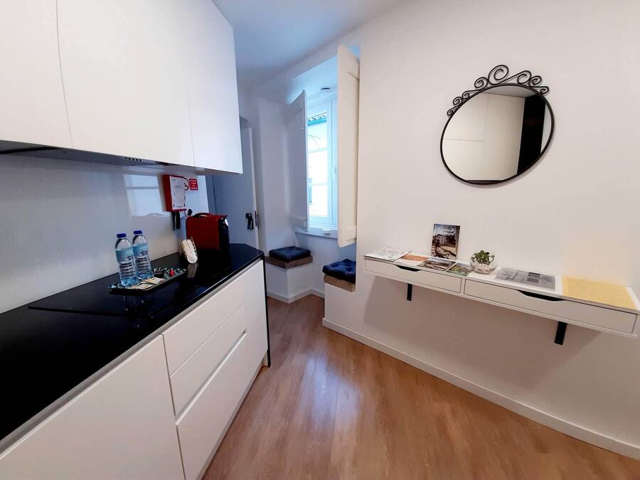 Een compacte keuken met witte kastjes, een zwart aanrecht en een klein eiland met een spoelbak en decoratieve objecten.